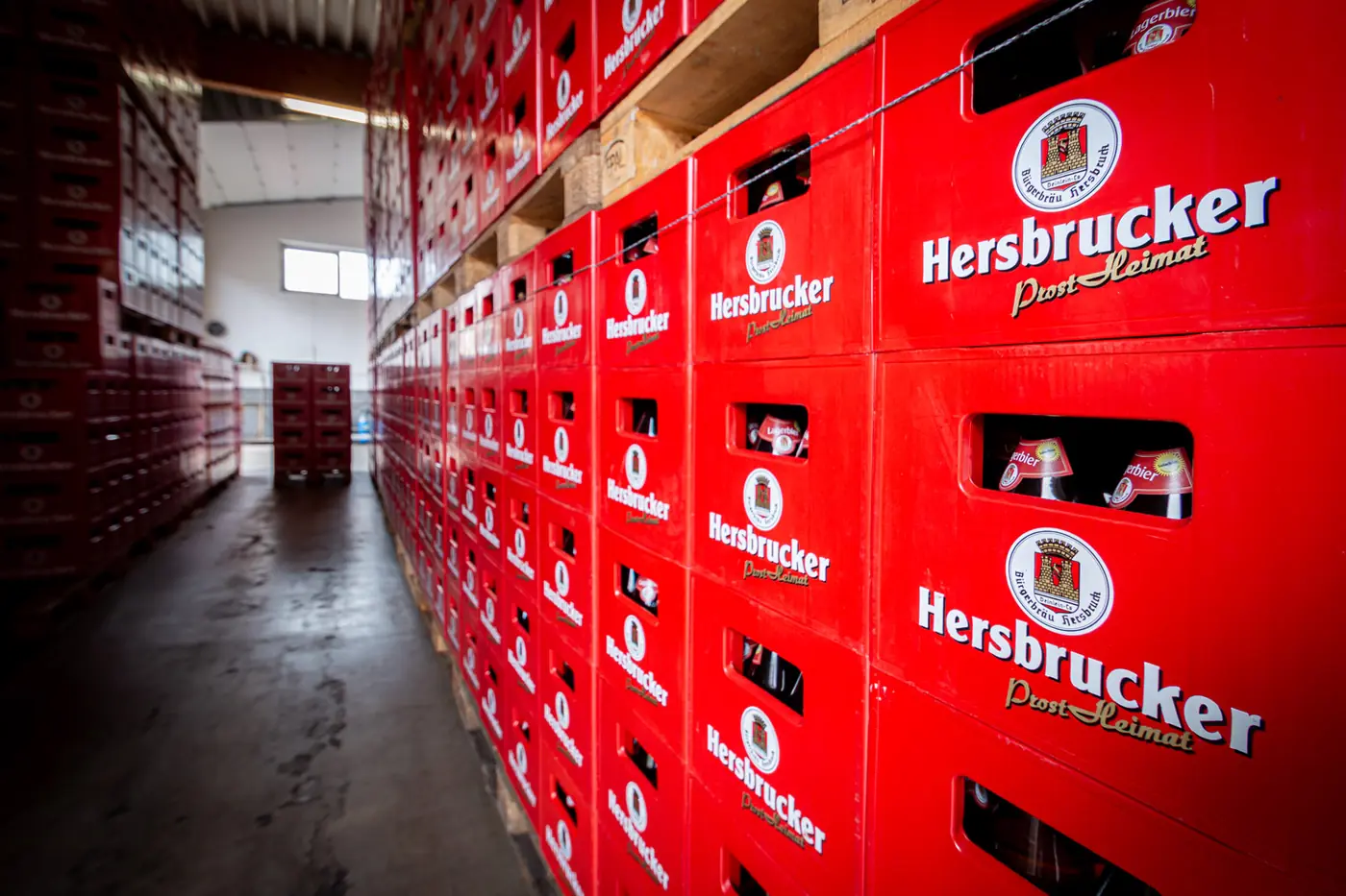 Gang zwischen hoch gestapelten roten Hersbrucker Kästen im Lager der Brauerei
